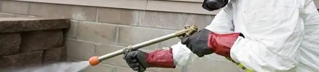 Pest control technician applying exterior insect treatment along a home foundation in Akron, OH