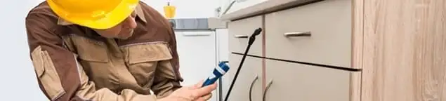 Roach exterminator applying treatment under kitchen cabinets in Akron, OH