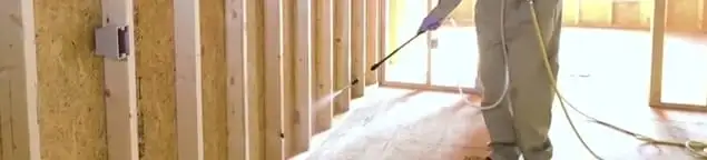 Termite treatment technician applying spray along framing and unfinished walls in Akron, OH